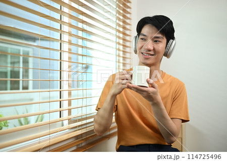 Portrait of positive man in wireless headphone drinking coffee and looking away 114725496