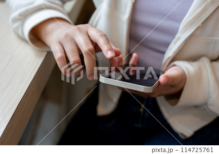 A close-up image of a woman in casual wear using her smartphone at a table indoors. A close-up image of a woman in casual wear using her smartphone at a table indoors. 114725761