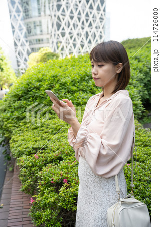 歩道脇で携帯を操作する女性 114726000