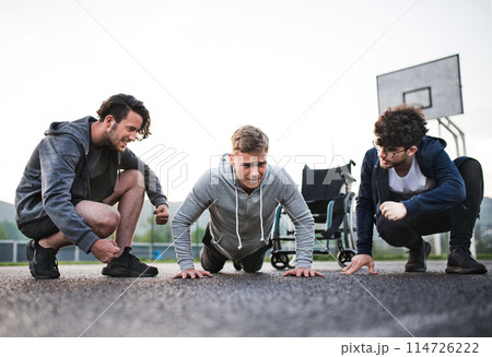 Disabled young man exercising with his supportive friends. Male friendship. Disabled young man exercising with his supportive friends. Male friendship. 114726222
