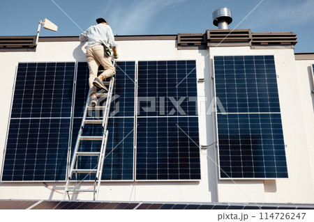 Man installing solar panels on the roof of his house 114726247