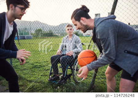 Disabled young man feeling excluded, want to play basketball with his friends, but because of wheelchair he can't. 114726248