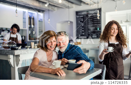 Beautiful female barista working in coffee shop, serving customers, elderly couple. University student working part-time in cafe. 114726335