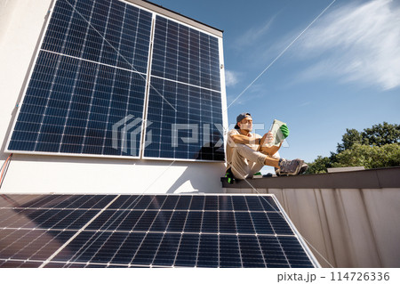 Man sitting on a rooftop with solar panels and using digital tablet 114726336