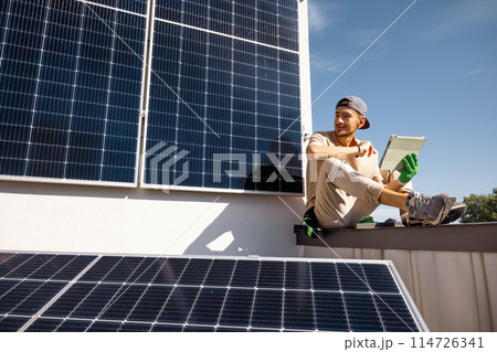 Man sitting on a rooftop with solar panels and using digital tablet 114726341