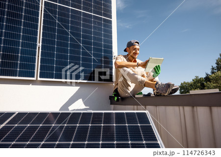 Man sitting on a rooftop with solar panels and using digital tablet 114726343