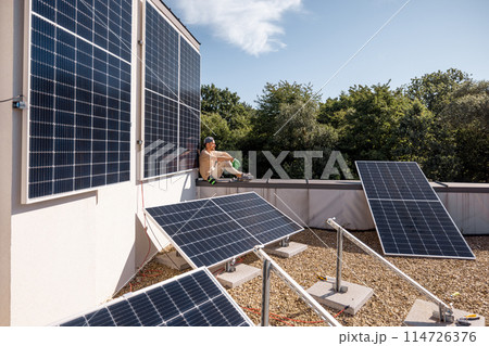 Man on a rooftop of his house with a solar power station 114726376