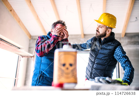 Colleague giving first aid to worker with chemical splashed on his skin, face. Accident at construction site Concept of occupational safety and health in workplace. 114726638
