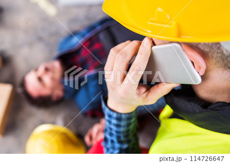 Colleague giving first aid to unconscious worker after accident, calling ambulance. Concept of occupational safety and health in workplace. Colleague giving first aid to unconscious worker after accident, calling ambulance. Concept of occupational safety and health in workplace. 114726647