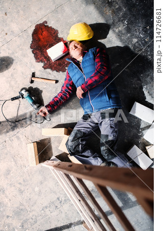 An unconscious man worker lying on the floor after a head injury. Work injury, accident in workplace. An unconscious man worker lying on the floor after a head injury. Work injury, accident in workplace. 114726681