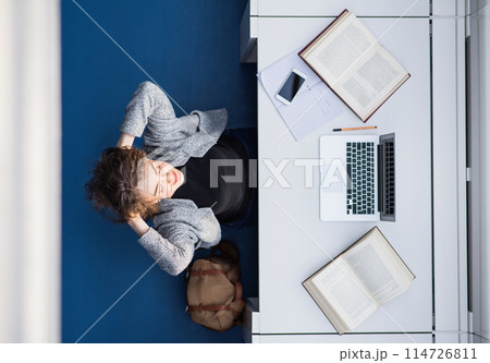 Top view of female student in library, taking break while preparing for final project, presentation. University student preparing for final exam. Top view of female student in library, taking break while preparing for final project, presentation. University student preparing for final exam. 114726811