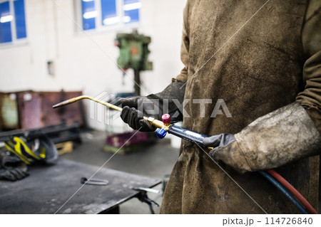 Beautiful blonde woman works as a welder in workshop, operating welding machine, wearing protective clothing and a welding mask. Beautiful blonde woman works as a welder in workshop, operating welding machine, wearing protective clothing and a welding mask. 114726840