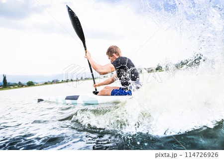 Canoeist man sitting in canoe holding paddle, in water. Concept of canoeing as dynamic and adventurous sport. Rear view, sportman looking at water surface, paddling Canoeist man sitting in canoe holding paddle, in water. Concept of canoeing as dynamic and adventurous sport. Rear view, sportman looking at water surface, paddling 114726926