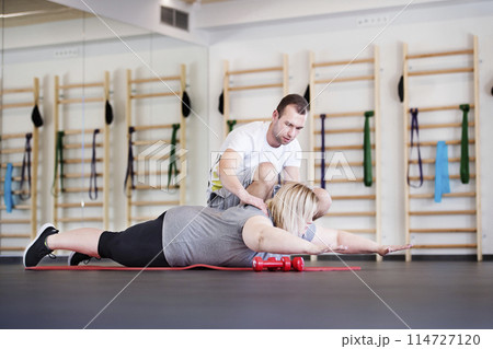 Overweight woman exercising on gym mat in gym. Personal trainer couching her and helping her. Overweight woman exercising on gym mat in gym. Personal trainer couching her and helping her. 114727120