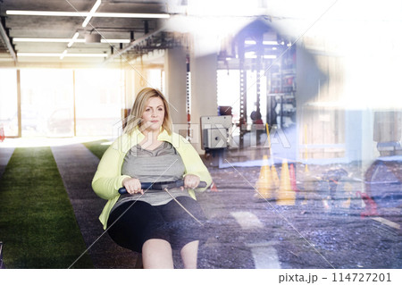 Overweight woman exercising on rowing machine. Routine workout for physical and mental health Overweight woman exercising on rowing machine. Routine workout for physical and mental health 114727201