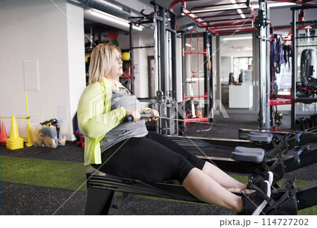 Overweight woman exercising on rowing machine. Routine workout for physical and mental health 114727202