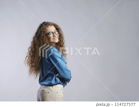 Portrait of a gorgeous teenage girl with curly hair and eyeglasses. Studio shot, white background with copy space 114727577