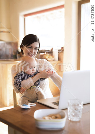 Mother with small baby working from homeoffice, typing on laptop. Mom paying bills online, holding small baby. 114727659