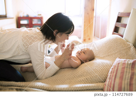 Mother playing with small baby lying on bed. Unconditional paternal love, mother's Day concept. 114727689