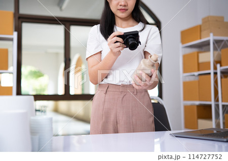 Young Asian business entrepreneur using a compact digital camera take a photo of product for upload to website online shop. 114727752