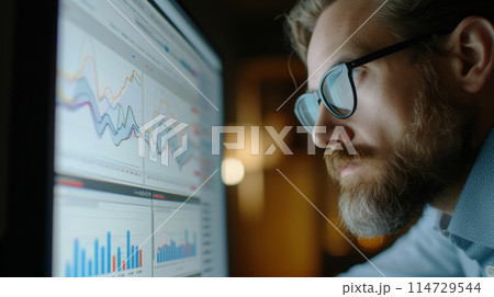An attentive man with glasses studies charts. An attentive man with glasses studies charts. 114729544