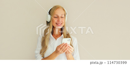 Happy smiling woman listening to music with phone in headphones on studio background 114730399