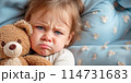 Child lying in bed with a teddy bear and crying. Family concept. 114731683