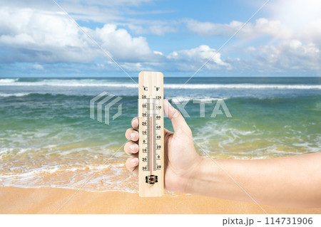 High temperature weather on summer seasons. Image of human hand holding thermometer on a beach with sunbeam. High temperature weather on summer seasons. Image of human hand holding thermometer on a beach with sunbeam. 114731906