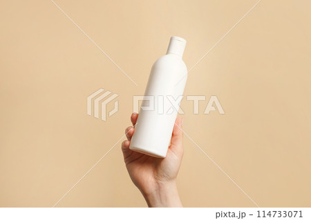 Hand holding white bottle of shampoo or hair conditioner on beige background, copy space Hand holding white bottle of shampoo or hair conditioner on beige background, copy space 114733071