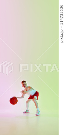 Dribbling. Full-length image of boy in uniform, playing basketball game, training against gradient background in neon light 114733536