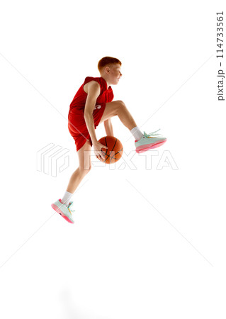 Full-length image of active teen boy in red uniform, basketball player training, playing isolated on white studio background Full-length image of active teen boy in red uniform, basketball player training, playing isolated on white studio background 114733561
