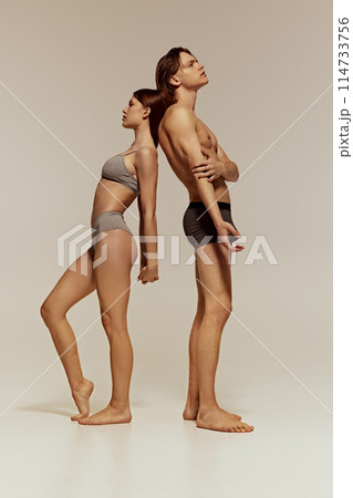Full-length image of young beautiful girl and handsome man, models with athletic fit bodies posing in underwear on grey studio background. Full-length image of young beautiful girl and handsome man, models with athletic fit bodies posing in underwear on grey studio background. 114733756