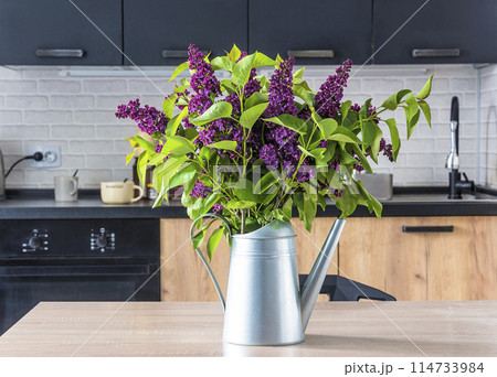 Bunch of purple lilac in watering can on a table in a kitchen 114733984