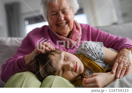 Sleeping girl lying head on gradmother knees. Portrait of an elderly woman spending time with granddaughter. 114734133