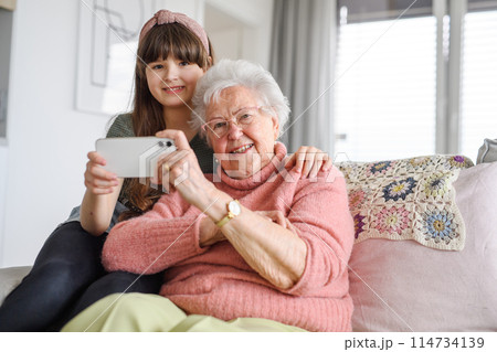 Grandmother with cute girl taking selfie with smartphone. Portrait of an elderly woman spending time with granddaughter. Grandmother with cute girl taking selfie with smartphone. Portrait of an elderly woman spending time with granddaughter. 114734139