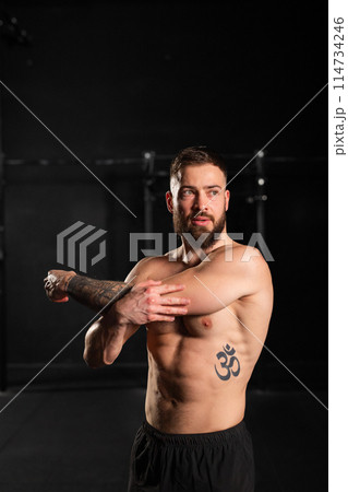 Portrait of handsome muscular man stretching before training in gym. Routine workout for physical and mental health. 114734246