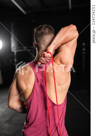 Rear view of handsome muscular man training with resistance band in gym. Routine workout for physical and mental health. Rear view of handsome muscular man training with resistance band in gym. Routine workout for physical and mental health. 114734251