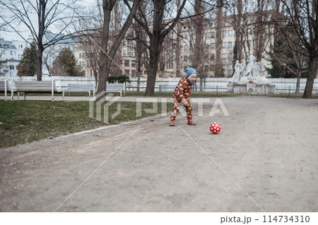 Cute toddler girl playing outdoor in playground with ball. Girl in softshell bodysuit spending time in park. 114734310