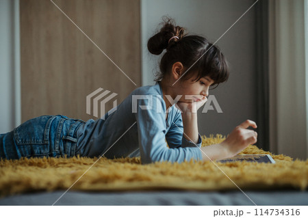 Cute girl lying on belly, scrolling on smartphone. Using social media. Side view. 114734316