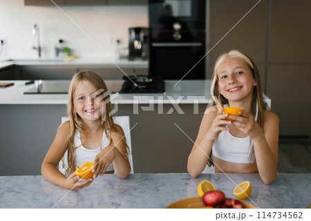 Two children sisters having breakfast and eating fresh oranges at the table in the kitchen 114734562