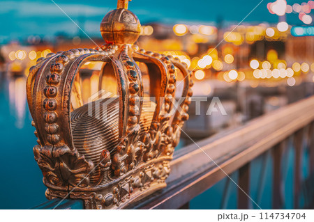 A gold crown on railing by waterside, surrounded by urban elements A gold crown on railing by waterside, surrounded by urban elements 114734704