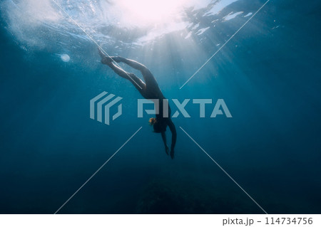 Silhouette of woman dive in transparent sea. Freediving with slim girl in ocean and sun rays Silhouette of woman dive in transparent sea. Freediving with slim girl in ocean and sun rays 114734756