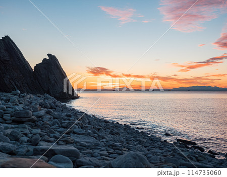 Sunset over rocky beach with silhouetted cliffs and calm ocean waters Sunset over rocky beach with silhouetted cliffs and calm ocean waters 114735060
