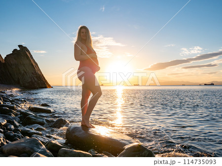 Pregnant woman enjoying sunset by the rocky beach during golden hour Pregnant woman enjoying sunset by the rocky beach during golden hour 114735093