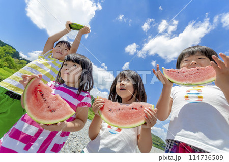 川原でスイカを食べる子供たち 114736509