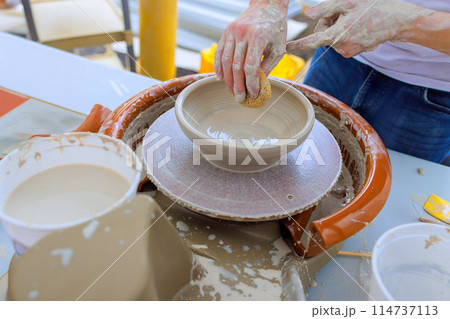 Using wet hands, ceramicist shapes soft clay on potter wheel 114737113