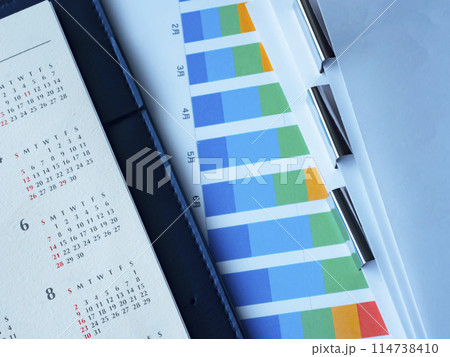 テーブルに置かれたグラフとカレンダーと書類と手帳 114738410