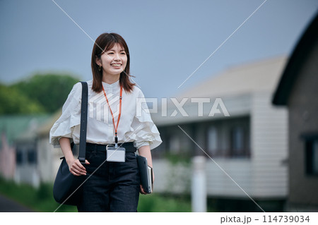 パソコンと手帳を持ちながら歩く若い女性 パソコンと手帳を持ちながら歩く若い女性 114739034