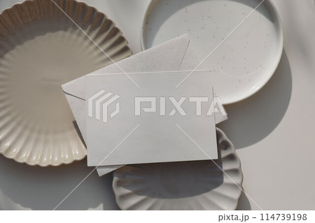 Empty horizontal greeting card, invitation mockup, envelope in sunlight. Various plates on beige table background. Soft shadows. Neutral still life, web banner. Food, restaurant, craft concept, flat Empty horizontal greeting card, invitation mockup, envelope in sunlight. Various plates on beige table background. Soft shadows. Neutral still life, web banner. Food, restaurant, craft concept, flat 114739198