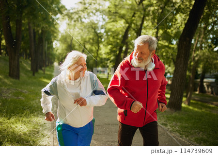 Senior Fitness Enthusiasts. Lively elderly couple, man and woman in sportswear running in park in the morning, growing energy and keeping toned 114739609